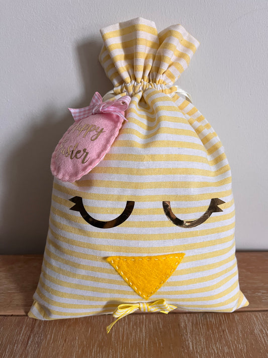 Yellow and white striped fabric bag with a chick face, pink Happy Easter tag, and small yellow bow.