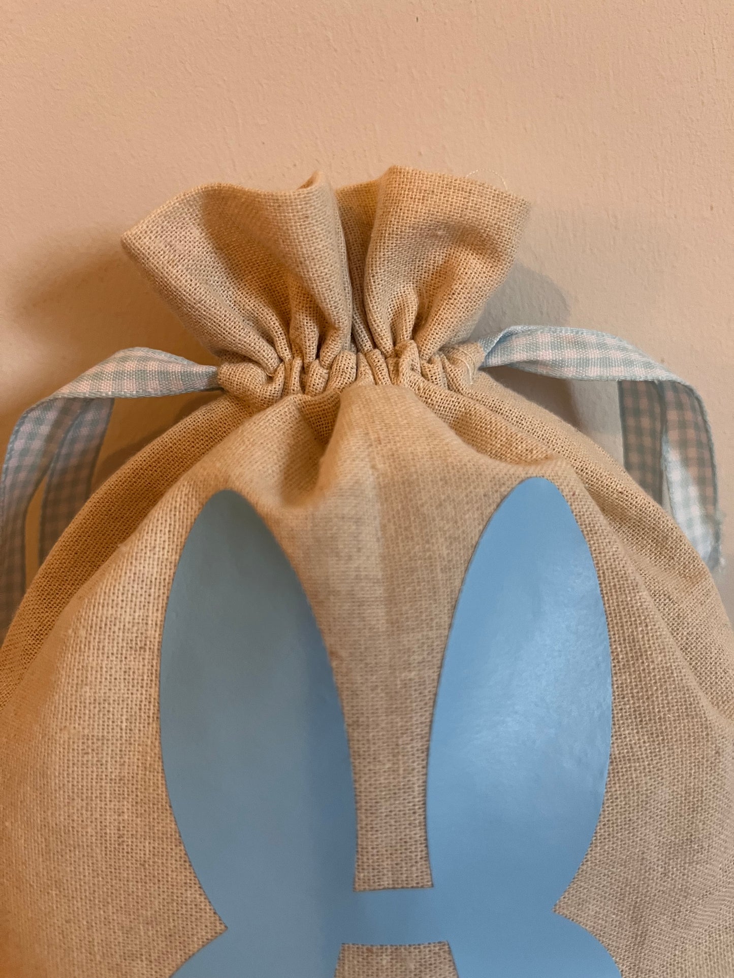 Close-up of a burlap drawstring bag with blue bunny ears and a checkered ribbon.