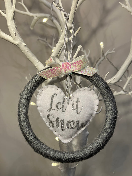 A gray yarn wreath with a white felt heart saying Let it Snow in the center.