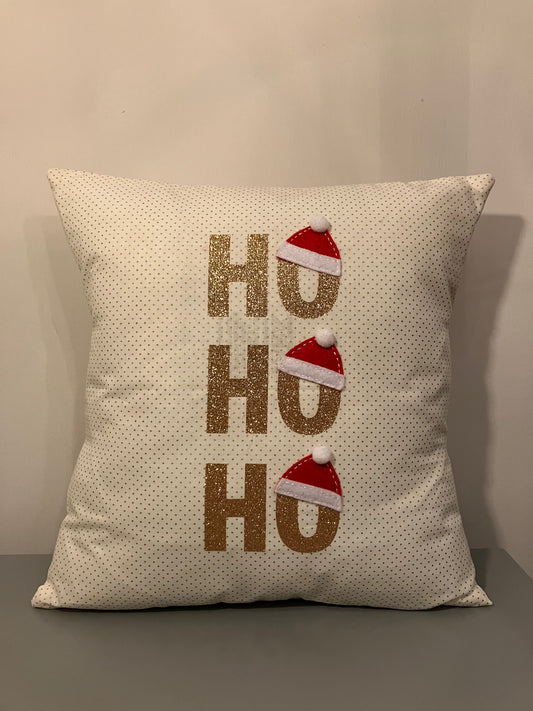 A festive pillow with the text HO HO HO in glittery gold, with Santa hats on the O's.