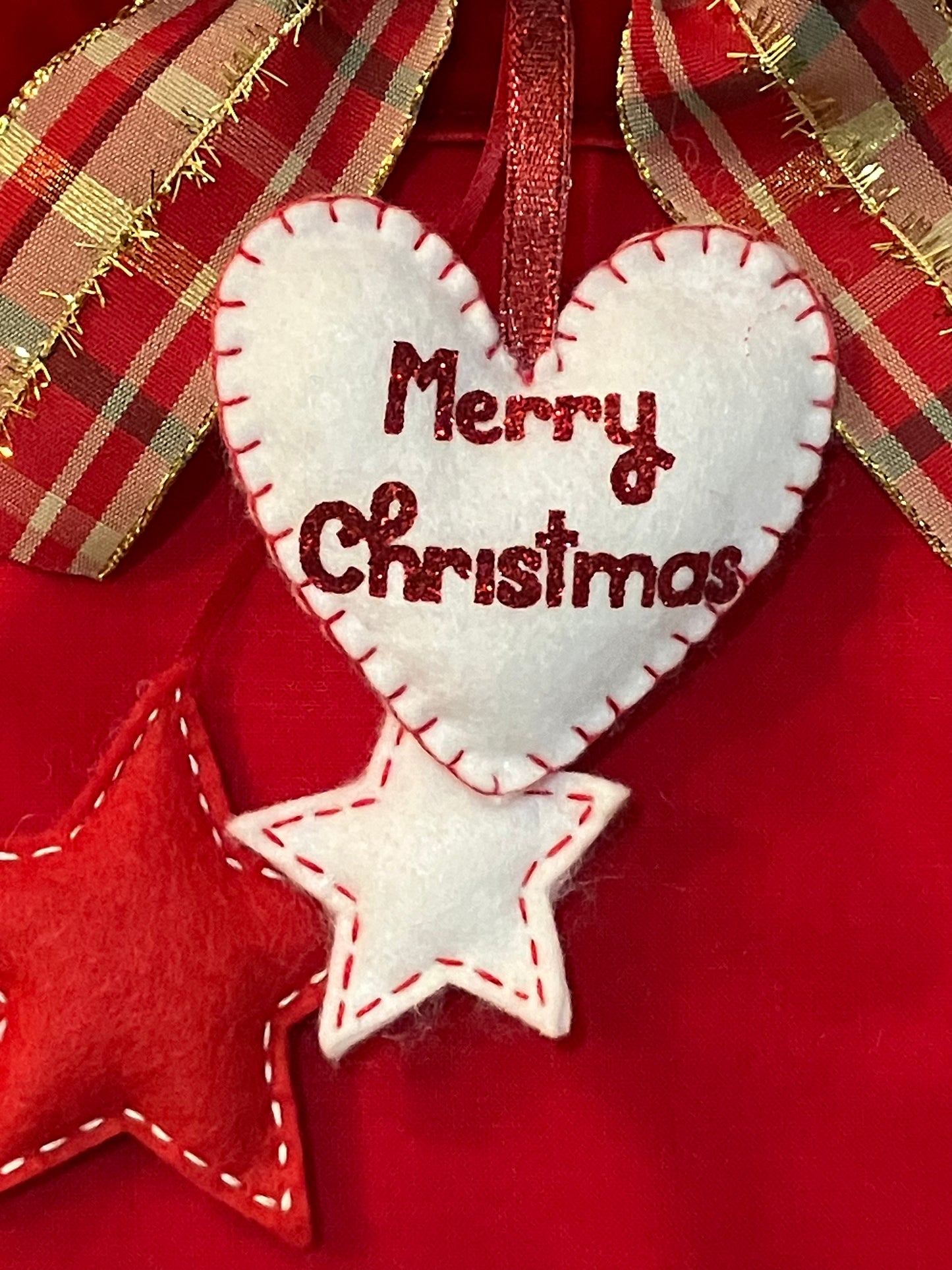A close-up of a white felt heart with "Merry Christmas" in red, above two felt stars.