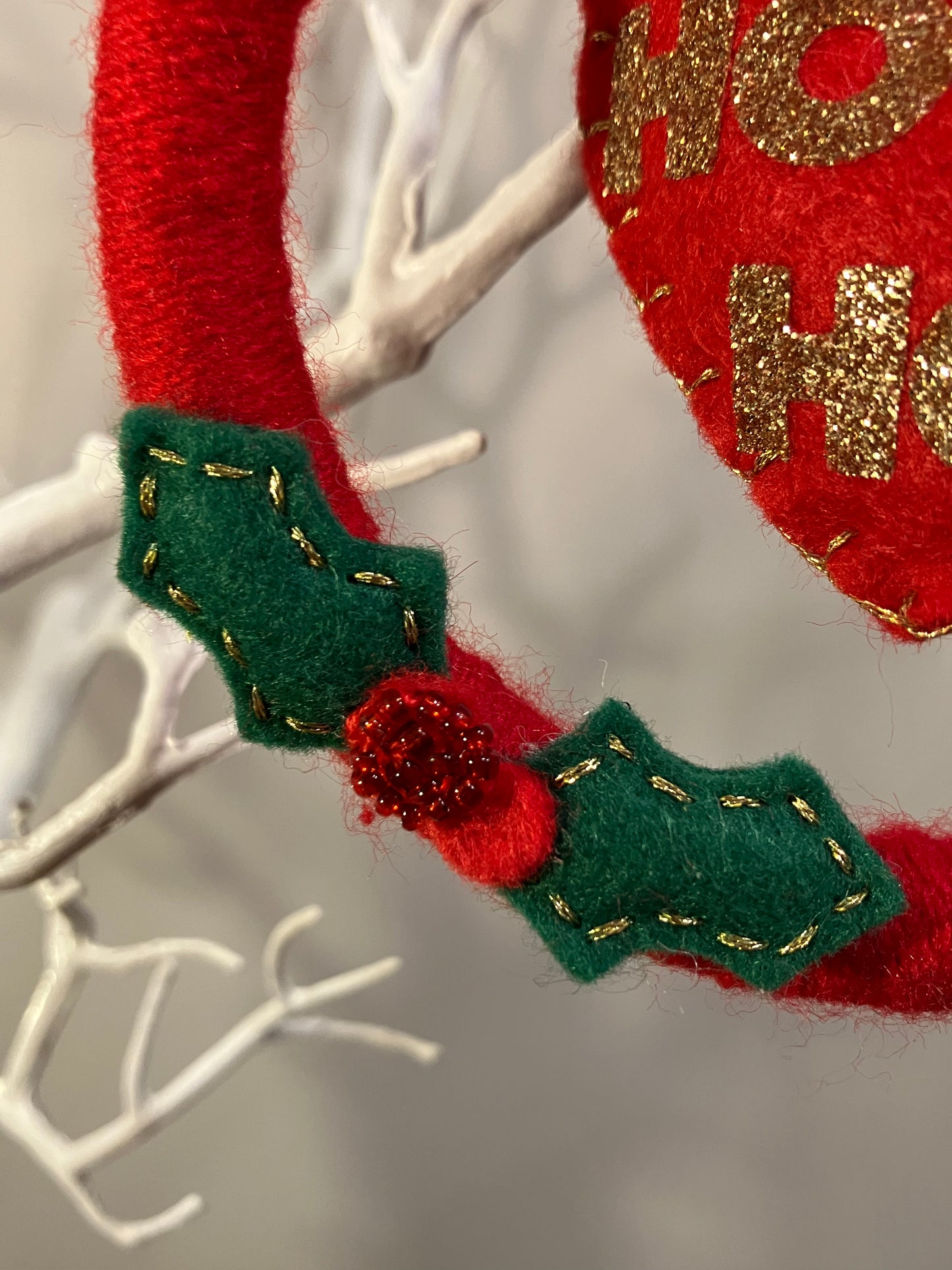 Bottom of the red felt wreath adorned with green holly leaves and red berries.