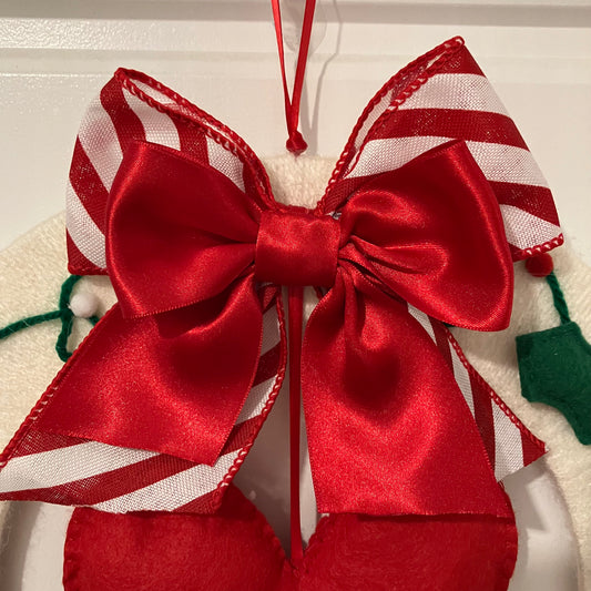A festive red and white striped bow with a solid red satin bow on top, hanging from a red ribbon.