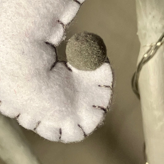 Close-up of a white felt ghost decoration with a small gray pom-pom nose and black stitching.