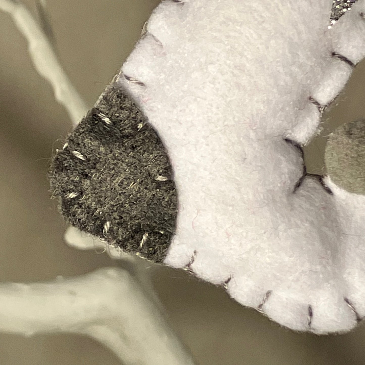 Close-up of a handmade white felt ornament with a dark gray tip and visible stitching.
