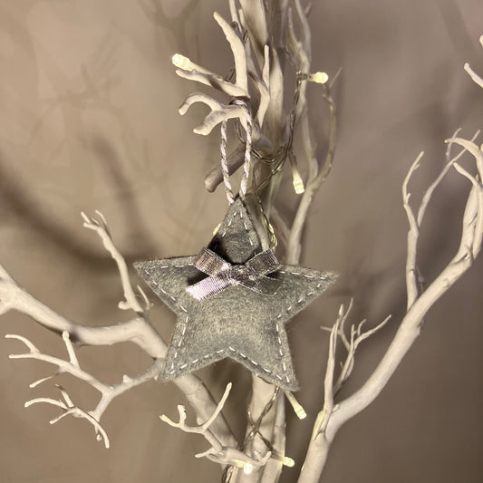 A grey felt star ornament with a silver bow hangs from a white decorative branch.