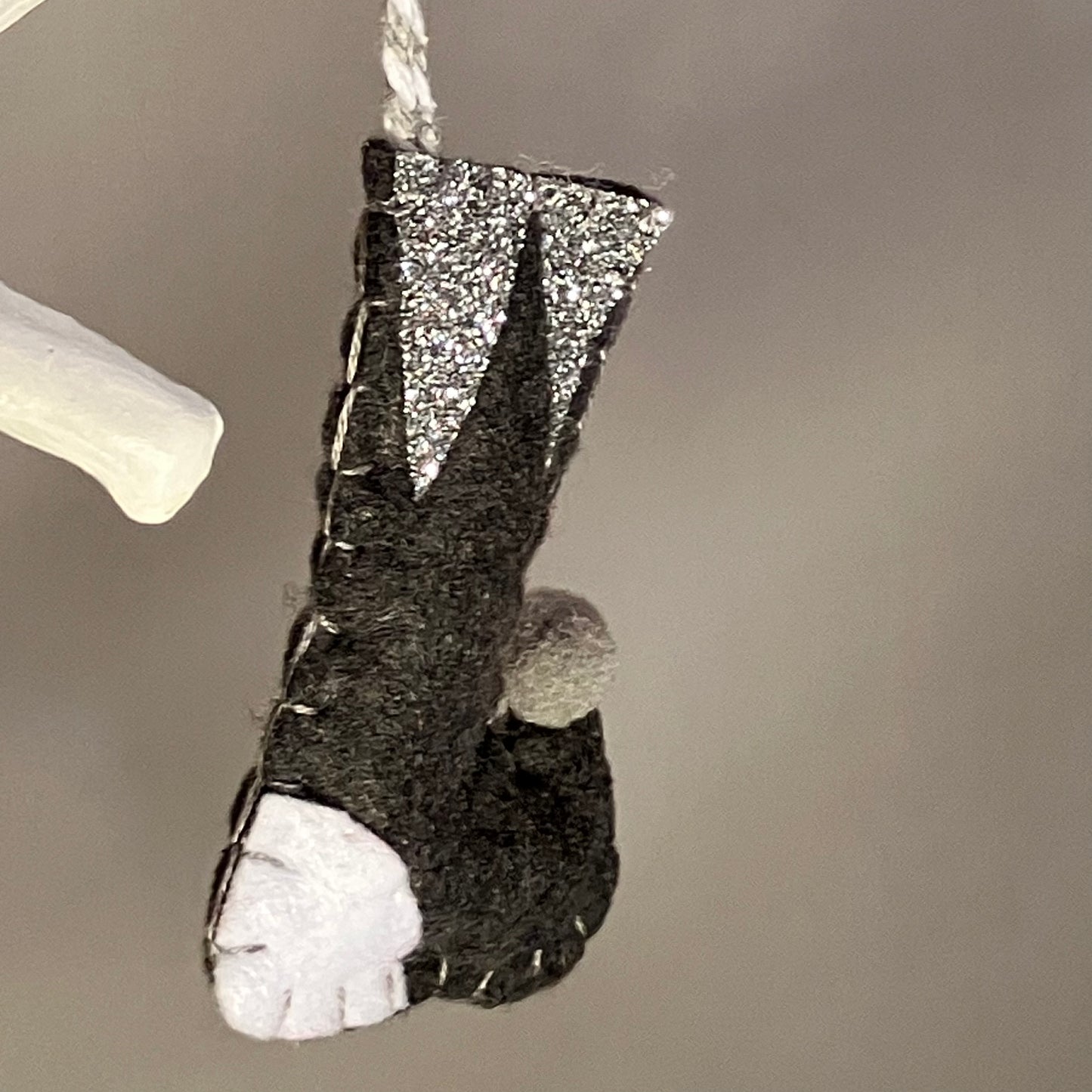Handmade black felt Christmas stocking ornament with glitter cuff and white toe.
