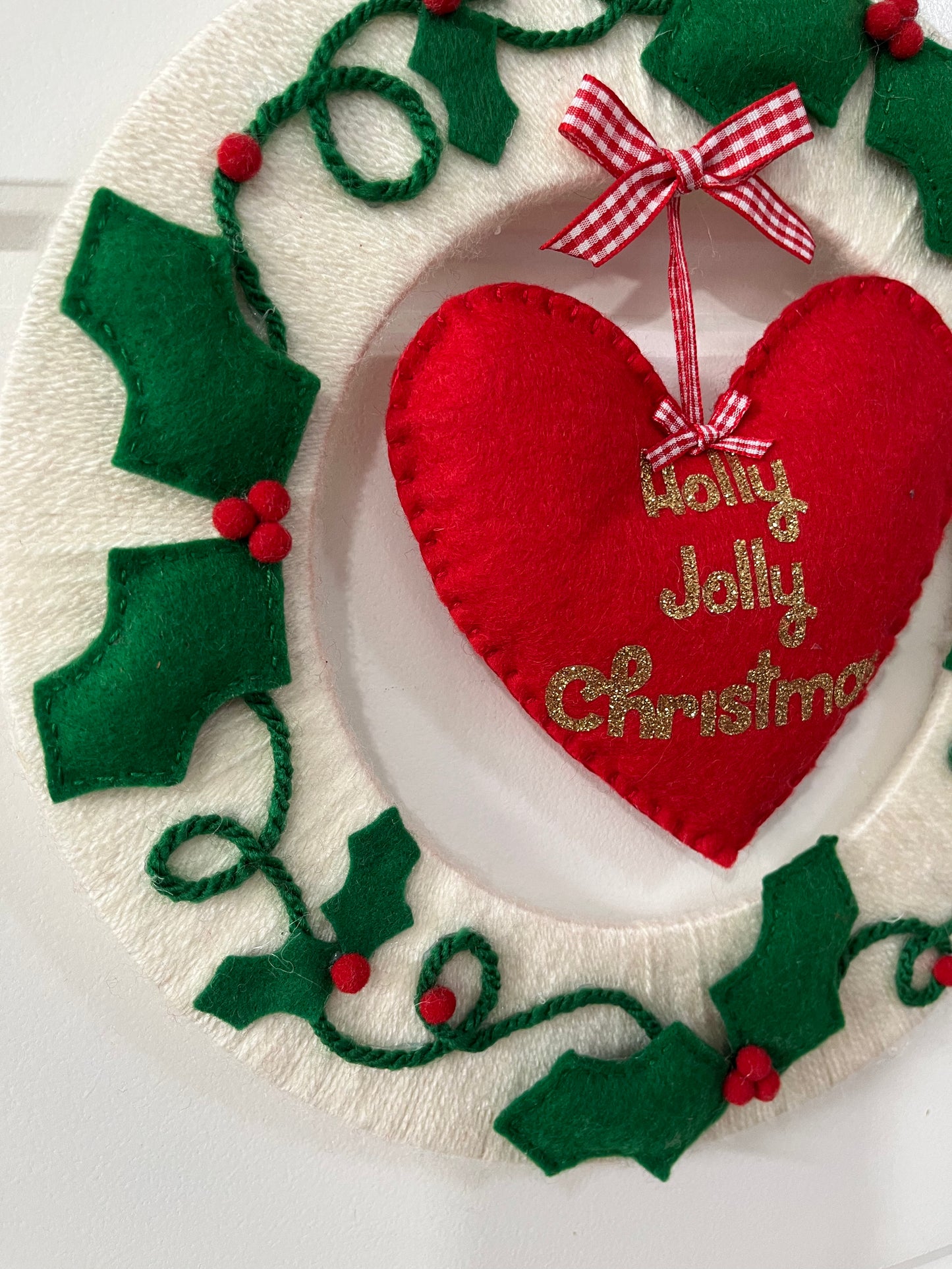 A close-up of a festive Holly Jolly Christmas wreath with a red heart and holly.