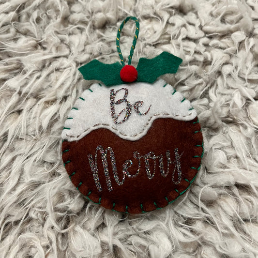 Handmade "Be Merry" Christmas pudding decoration on a white furry background.