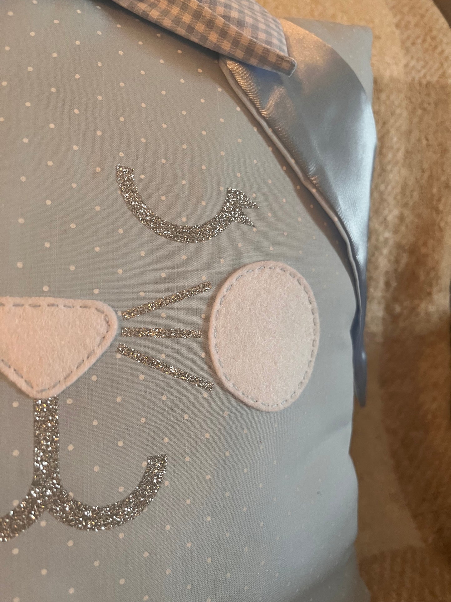 Close-up of a light blue pillow with white polka dots and a glittery cat face design.