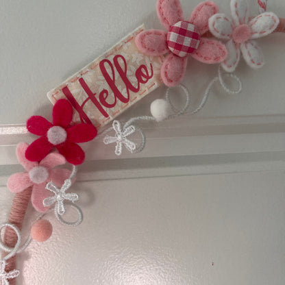 Close-up of a decorative felt wreath with pink and white flowers and a Hello banner.