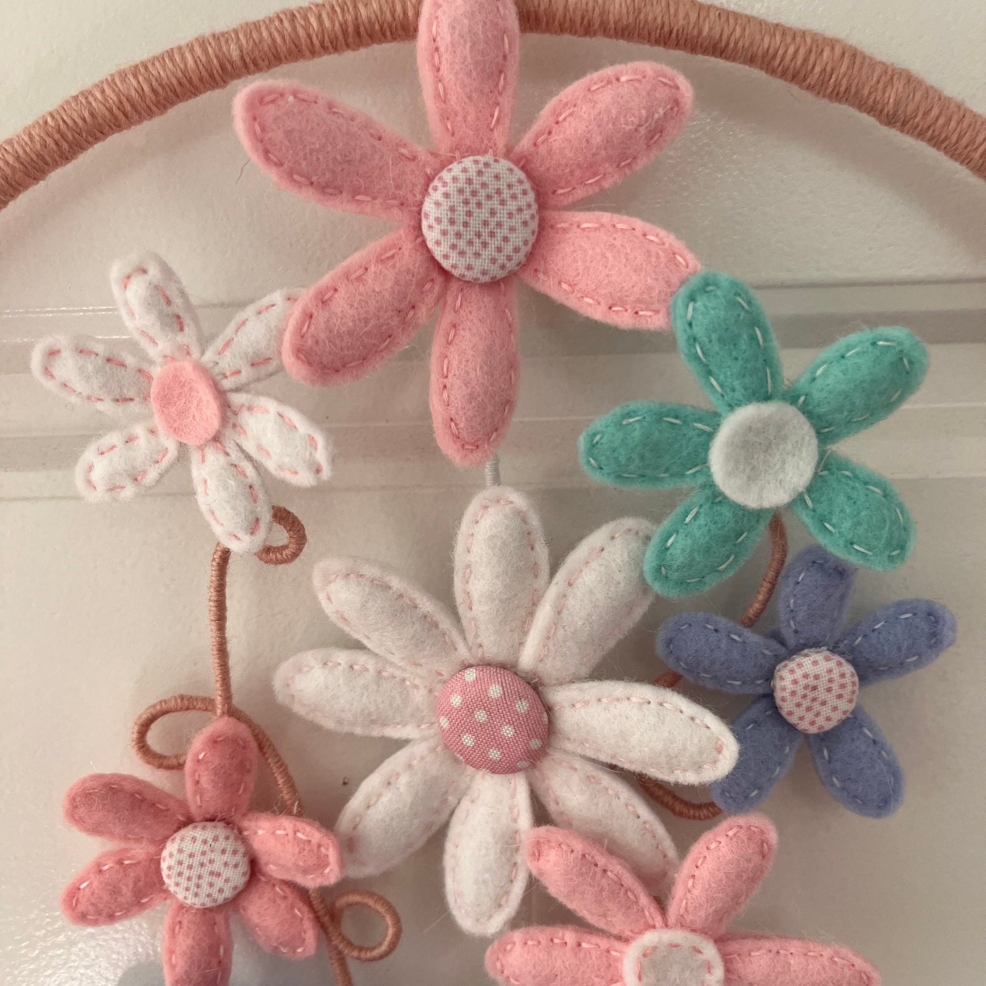 Close-up of a handmade felt flower mobile with pink, white, teal, and lavender flowers.