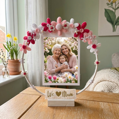 A white circular photo frame with pink and white felt flowers. It holds a photo of three generations of women.