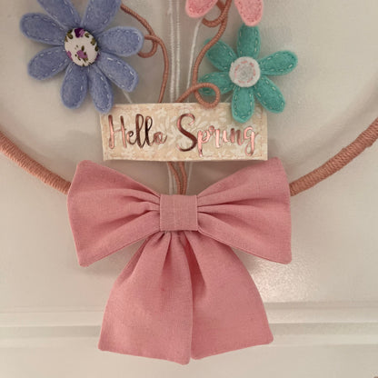 A Hello Spring sign with felt flowers and a pink bow.