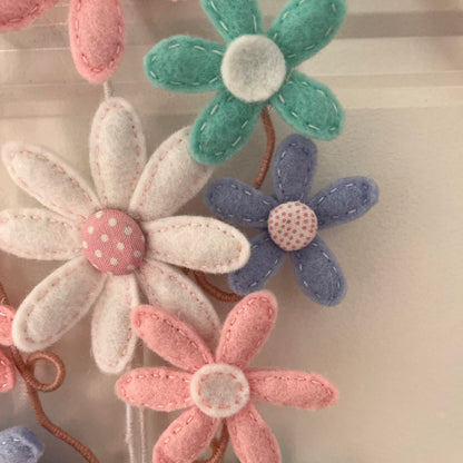 Close-up of handmade felt flowers in pink, white, teal, and purple with stitched details.