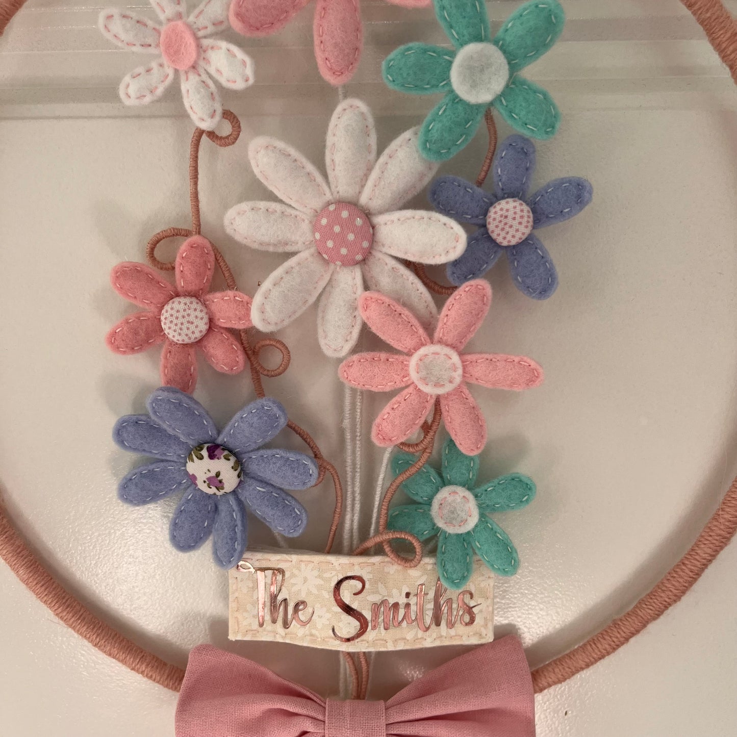 Close-up of a decorative hoop with felt flowers in pink, white, blue, and teal, and a The Smiths tag.