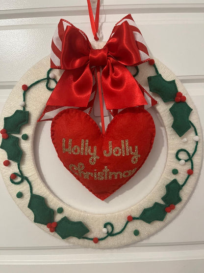 A white felt wreath with green holly leaves, red berries, and a red heart with "Holly Jolly Christmas".