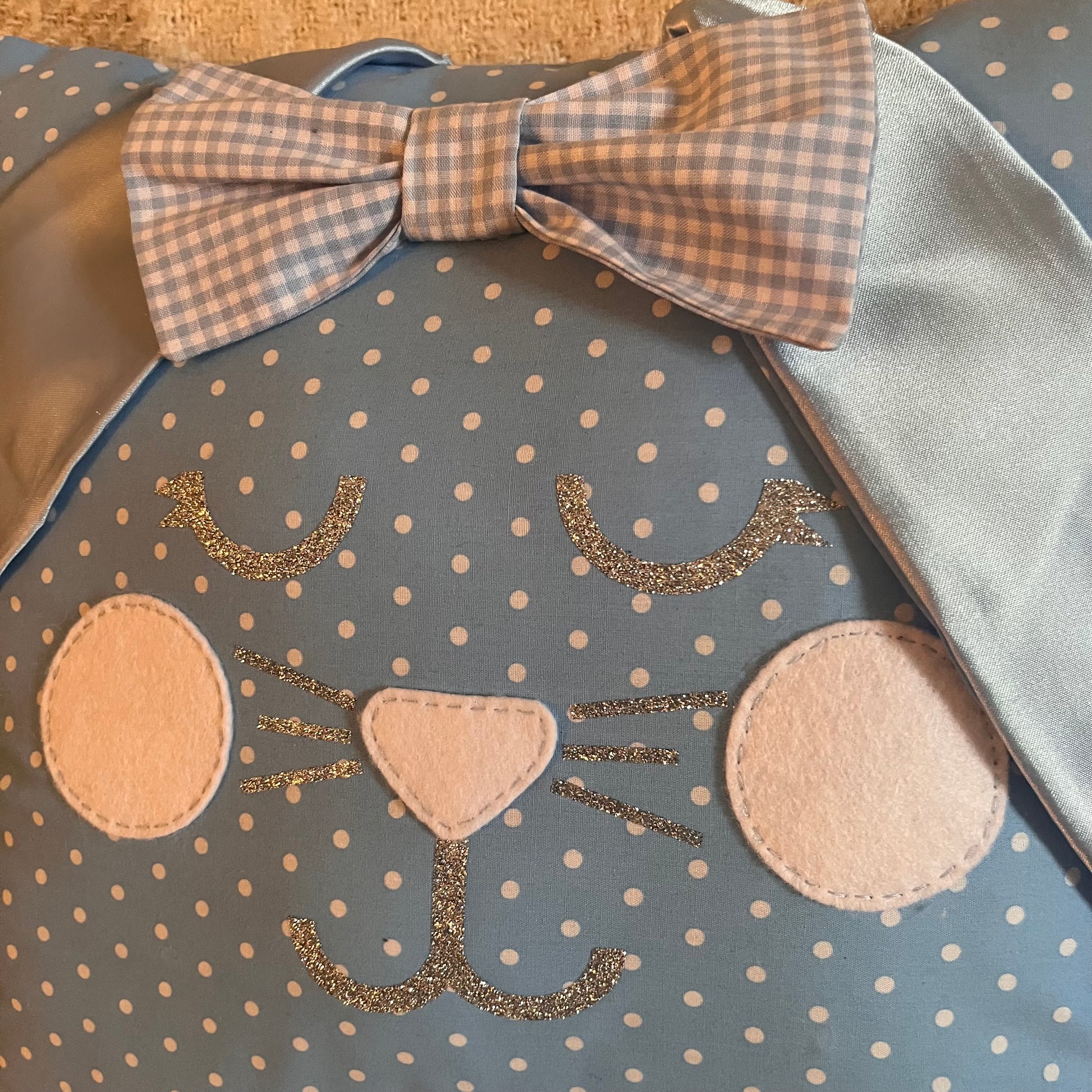 Close-up of a blue polka dot bunny pillow with a gingham bow and glitter details. 