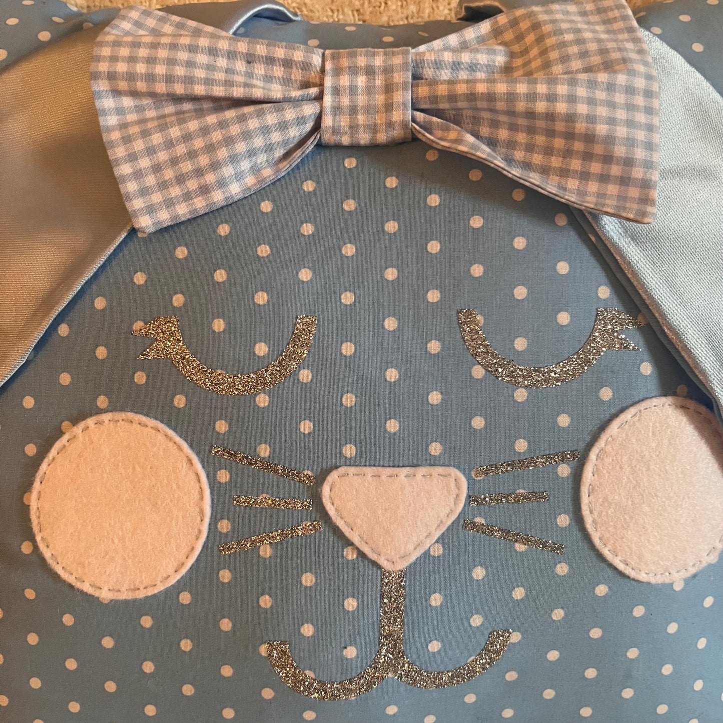 Close-up of a blue polka dot bunny pillow with a gingham bow, felt cheeks, and glitter whiskers.