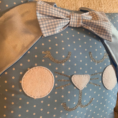 Blue polka dot pillow with a cat face, white felt cheeks, glitter whiskers, and a gingham bow.