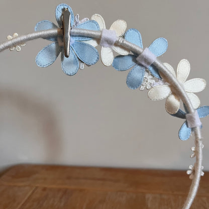 Close-up of a white headband adorned with blue and white fabric flowers, with a silver clip attached.