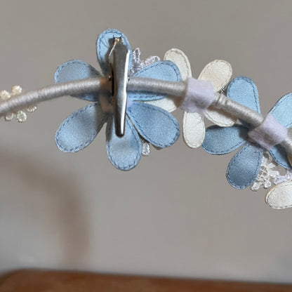 Close-up of a white headband with light blue and white fabric flowers, secured by a silver clip.