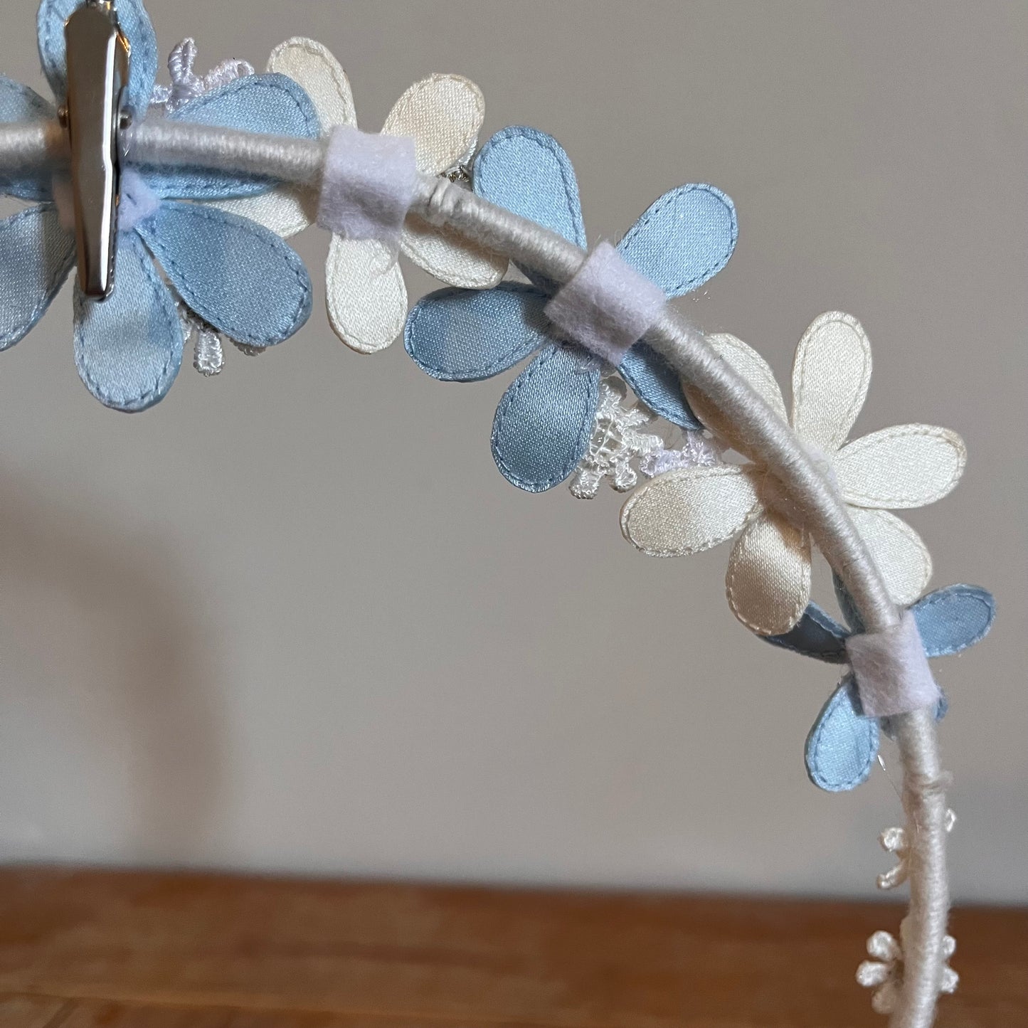 Close-up of a headband adorned with light blue and white fabric flowers, secured by a silver clip.