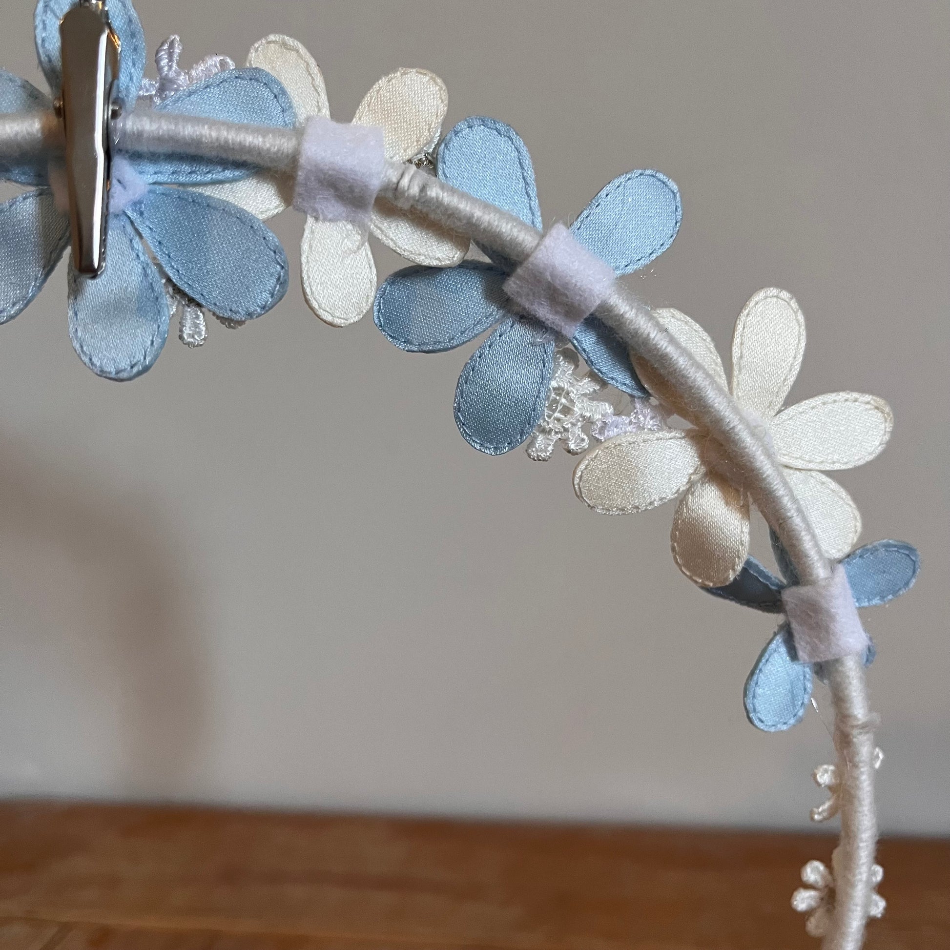 Close-up of a headband adorned with light blue and white fabric flowers, secured by a silver clip.