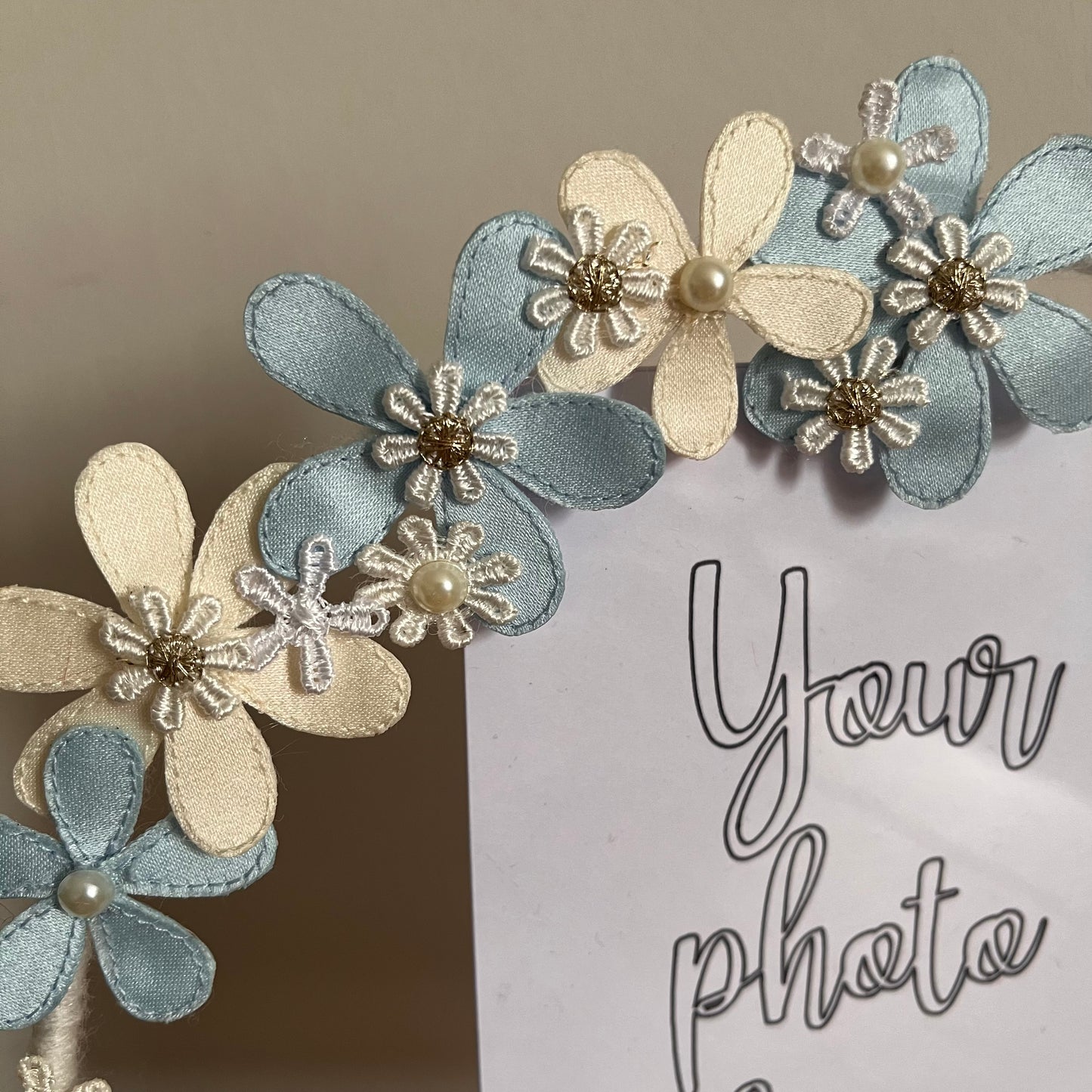 Close-up of a photo frame decorated with blue and cream fabric flowers, some with pearl centers.