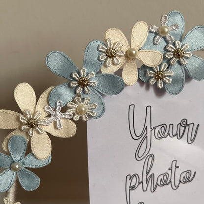 Close-up of a photo frame decorated with blue and cream fabric flowers, some with pearl centers.