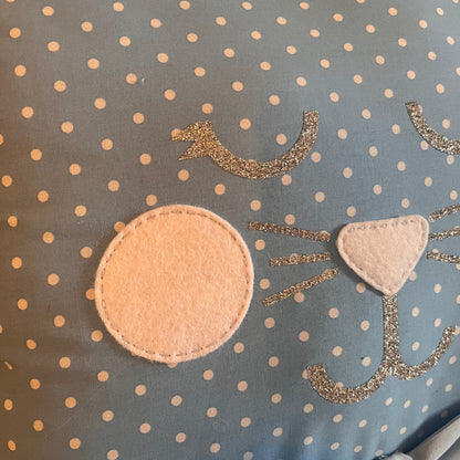 Close-up of a blue polka dot fabric with a cat face design made from felt and glitter.