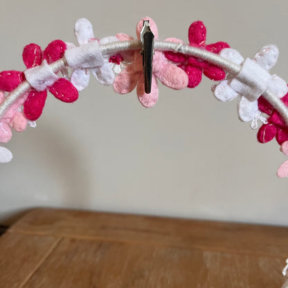 Close-up of a white headband adorned with pink, white, and fuchsia felt flowers, held by a silver clip.