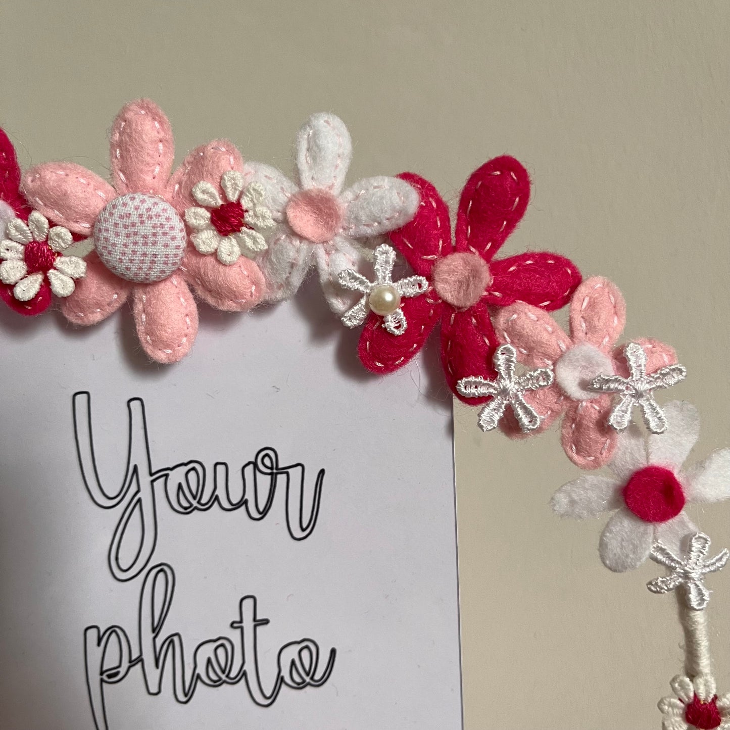Close-up of a photo frame adorned with felt flowers in shades of pink and white, with the text Your photo.