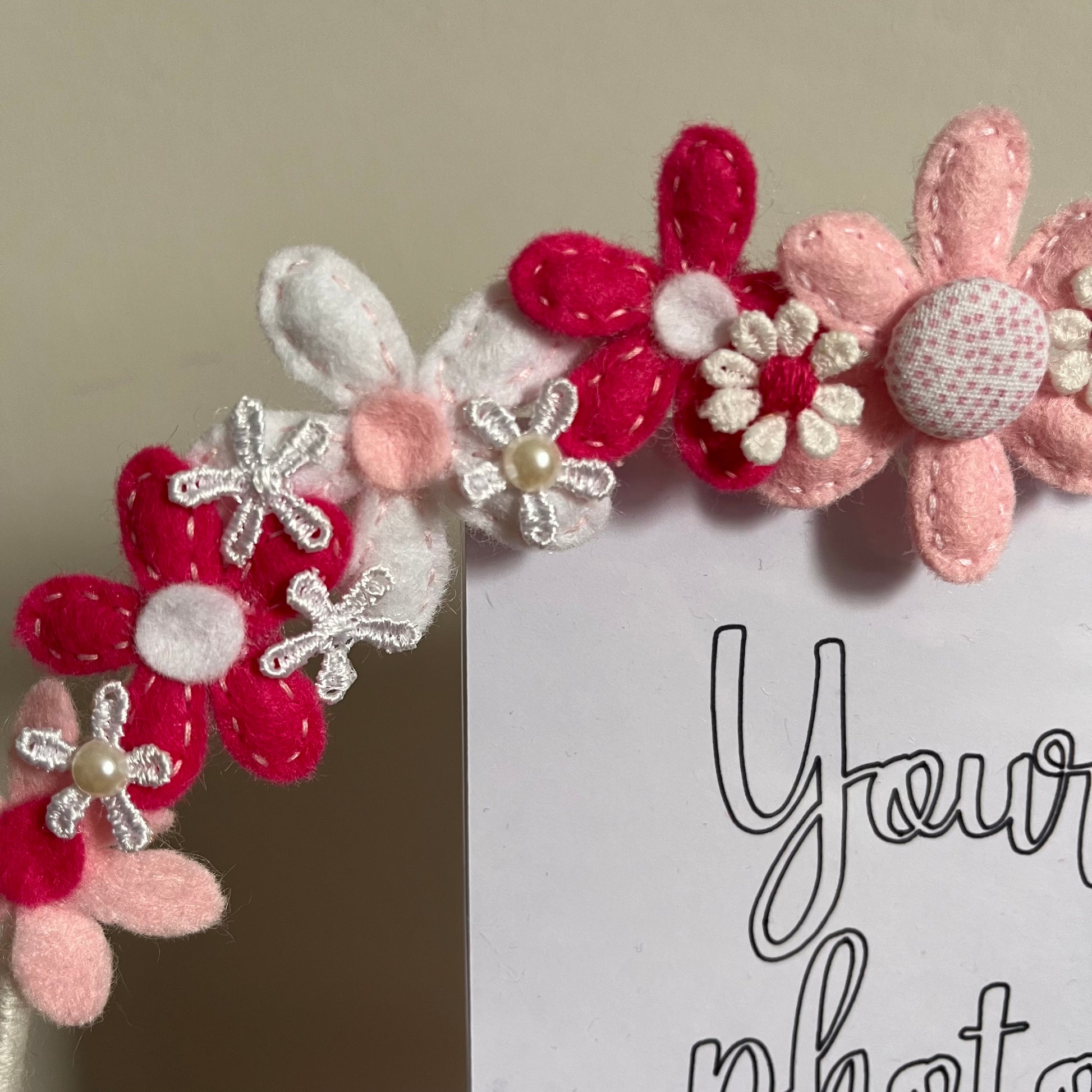 Close-up of a photo frame adorned with pink, white, and fuchsia felt flowers, some with pearl centers. 