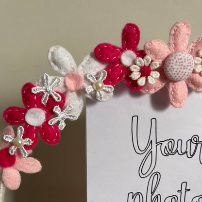 Close-up of a photo frame adorned with pink, white, and fuchsia felt flowers, some with pearl centers. 