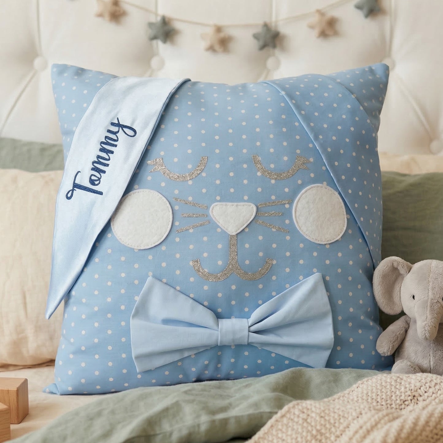 Blue polka dot bunny pillow with Tommy embroidered on ear, a blue bow, and a plush elephant.
