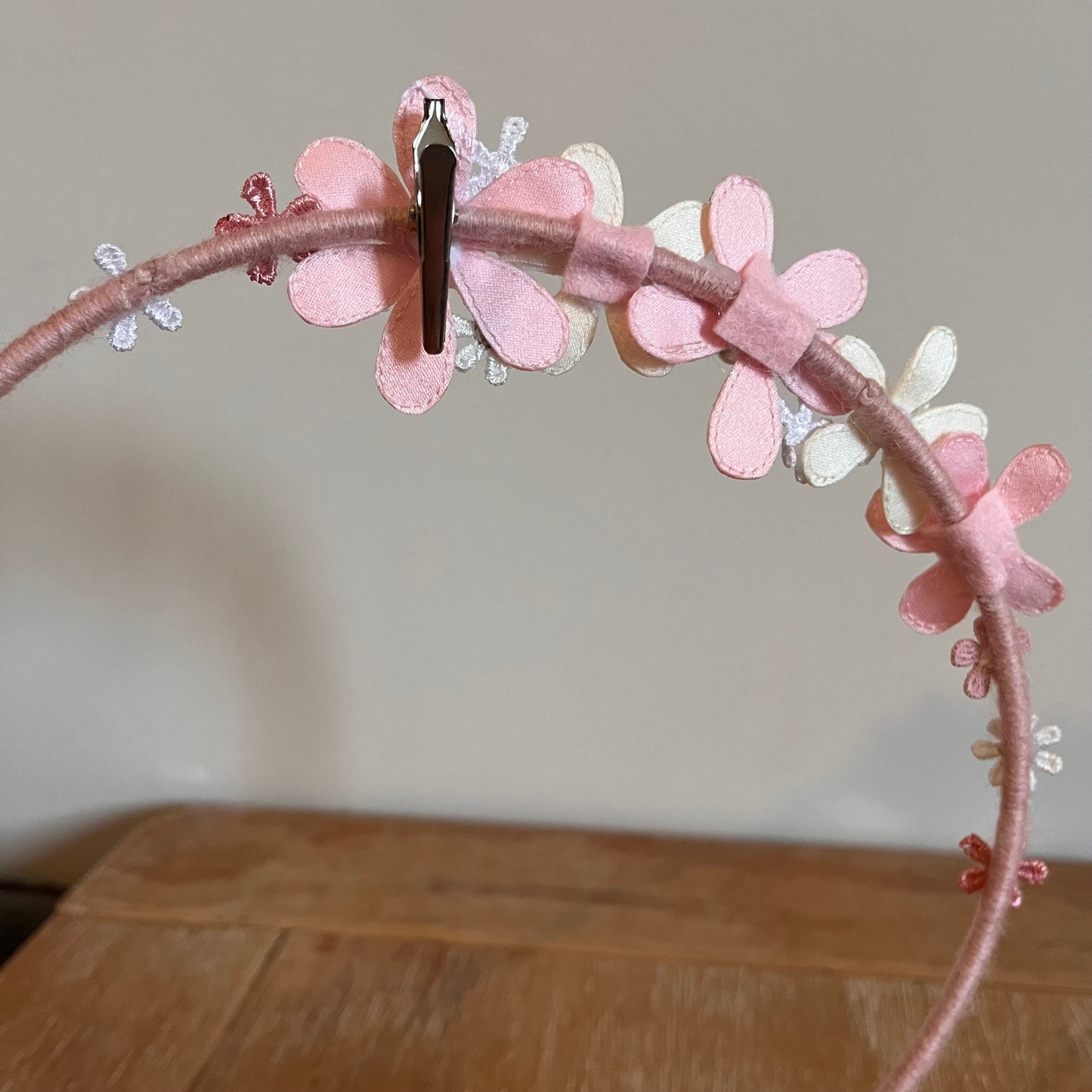 Pink headband with fabric flowers in various shades of pink and white, with a silver clip attached.