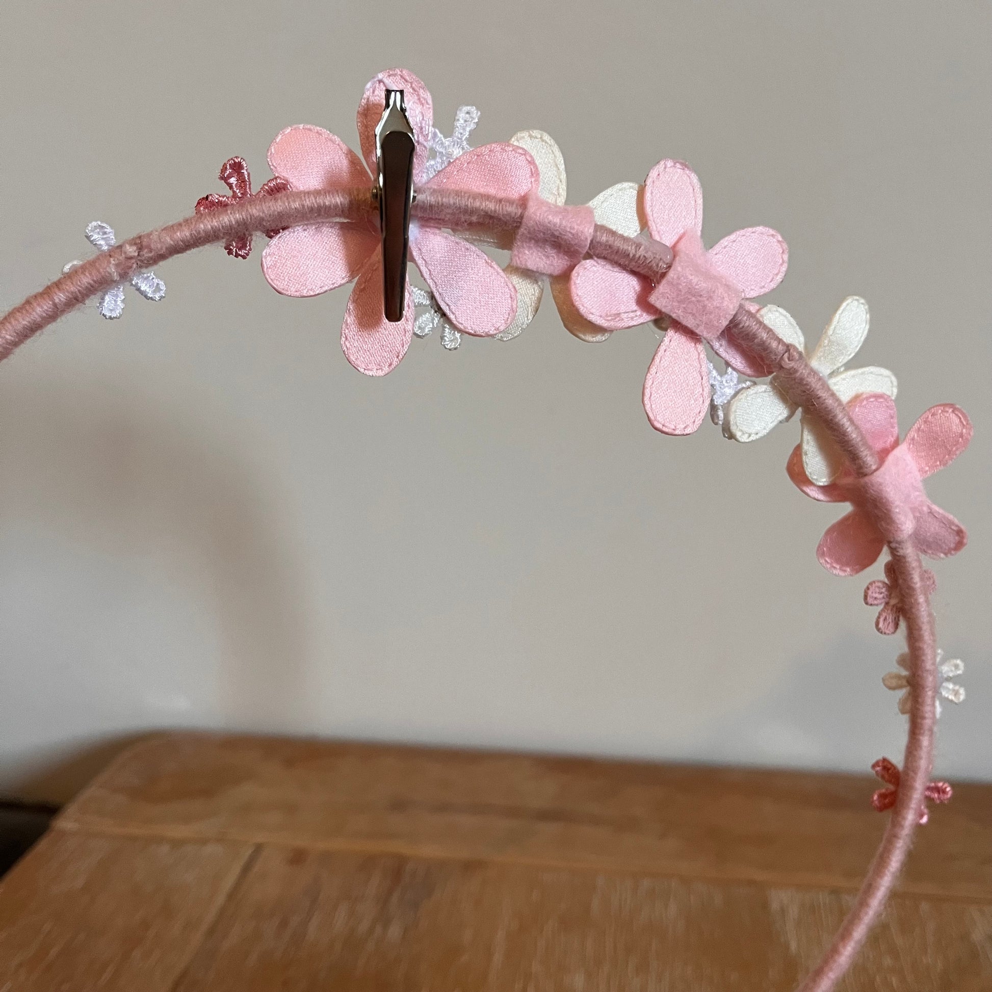 Pink headband with fabric flowers in various shades of pink and white, with a silver clip attached.