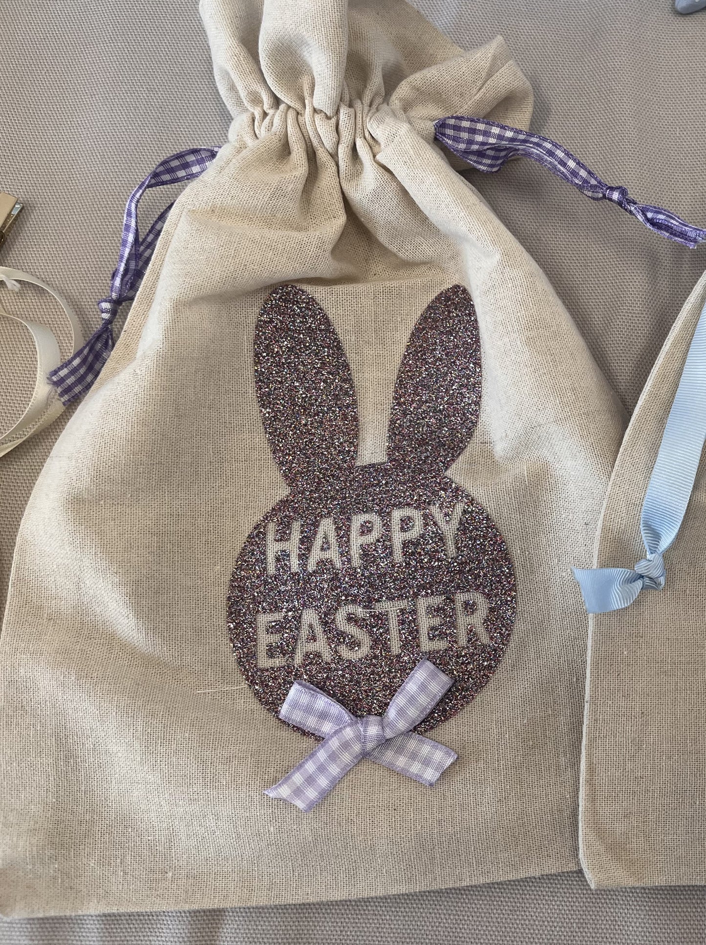 Easter bunny bag with glitter and purple gingham ribbon. Happy Easter is written on the bag.