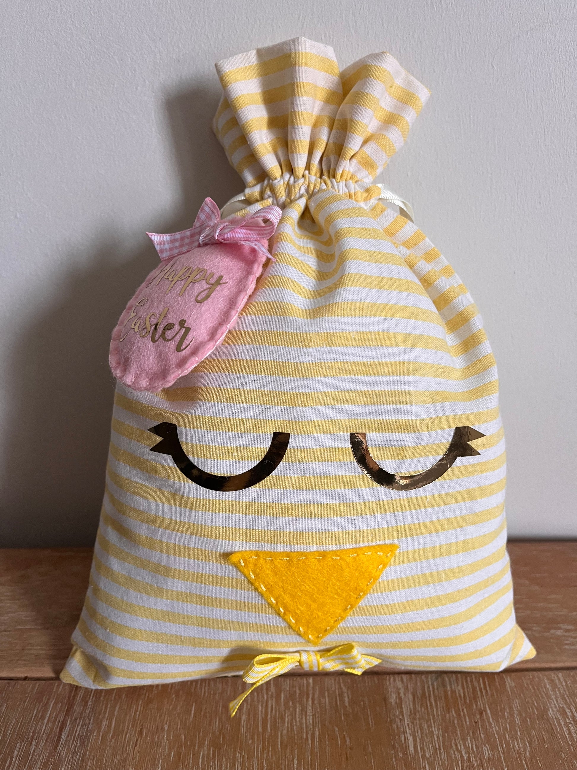 Yellow and white striped fabric bag with a chick face, pink Happy Easter tag, and small yellow bow.