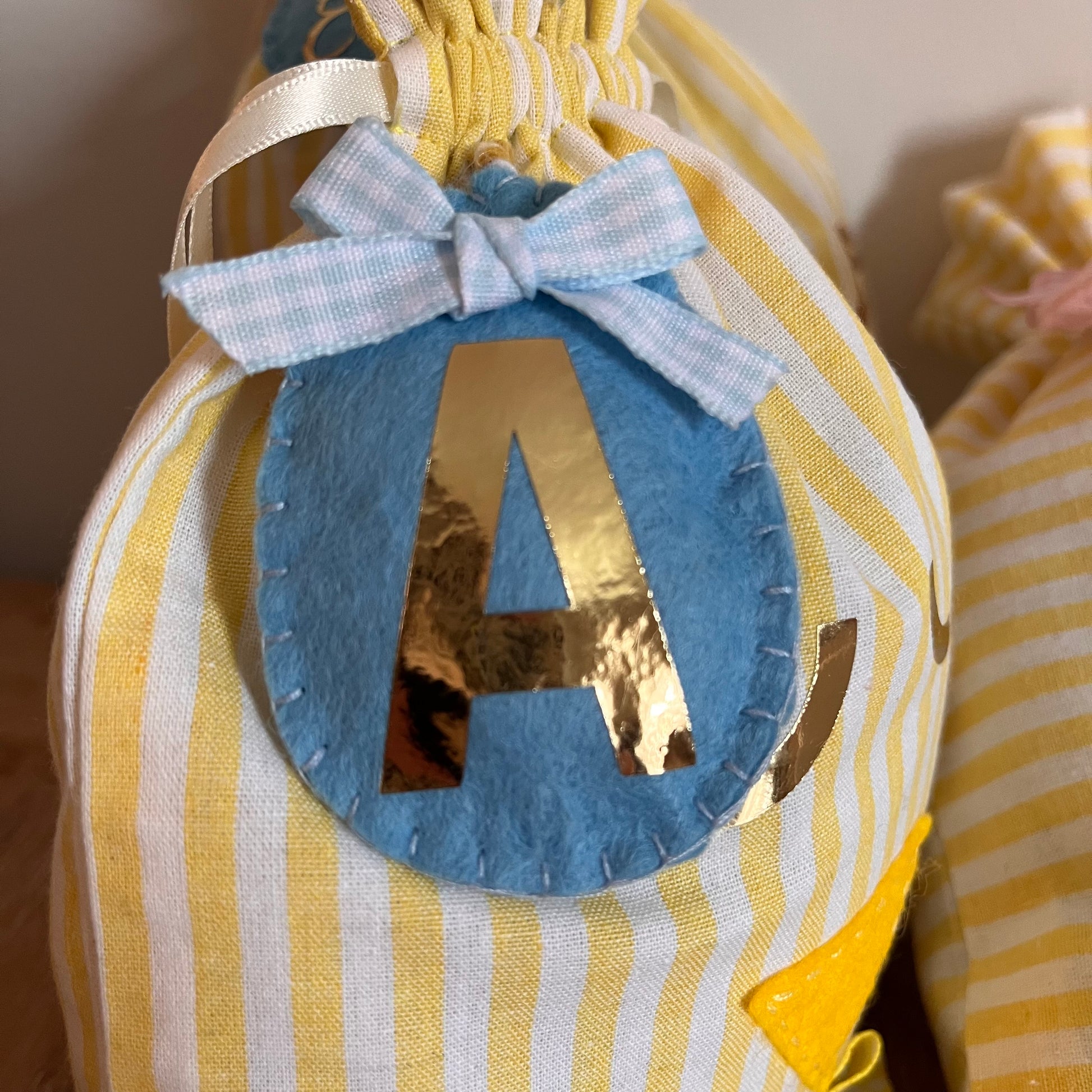 Close-up of a yellow and white striped fabric bag with a blue felt circle and a golden letter A.