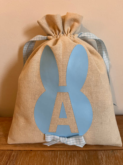 Burlap Easter bag with blue bunny ears and the letter A, tied with a blue gingham ribbon.