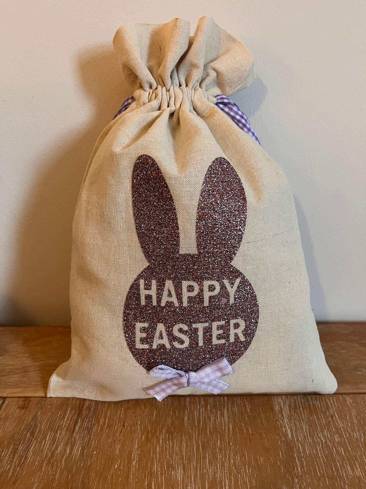 Happy Easter burlap bag with glitter bunny ears and a purple gingham bow.