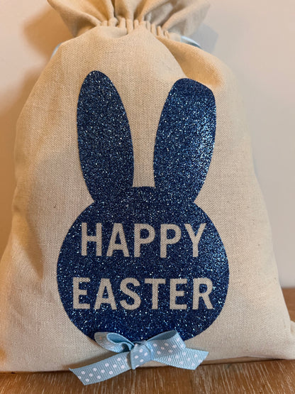 A beige drawstring bag with a blue glitter bunny silhouette and Happy Easter text.