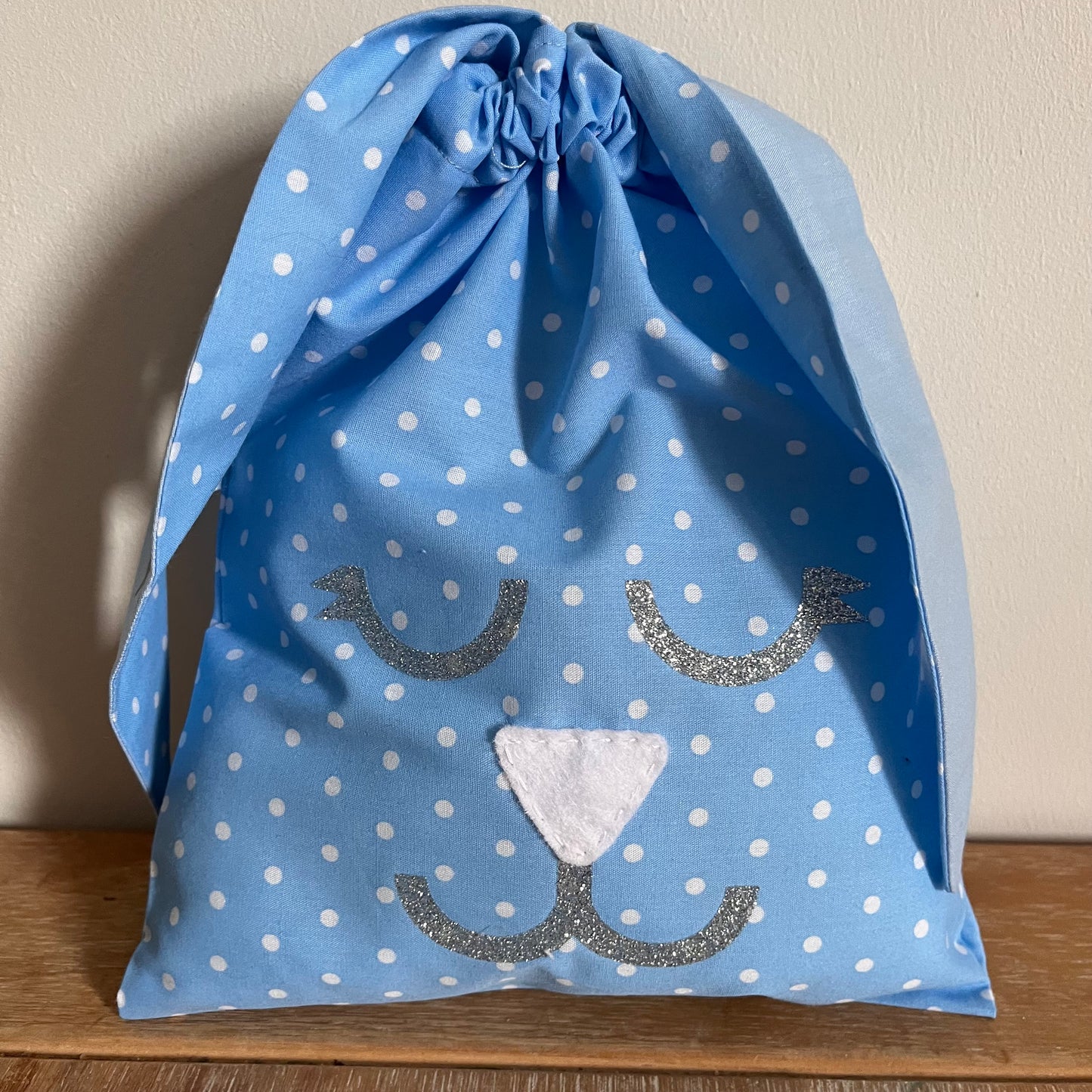 Blue polka dot drawstring bag with a glittery bunny face design