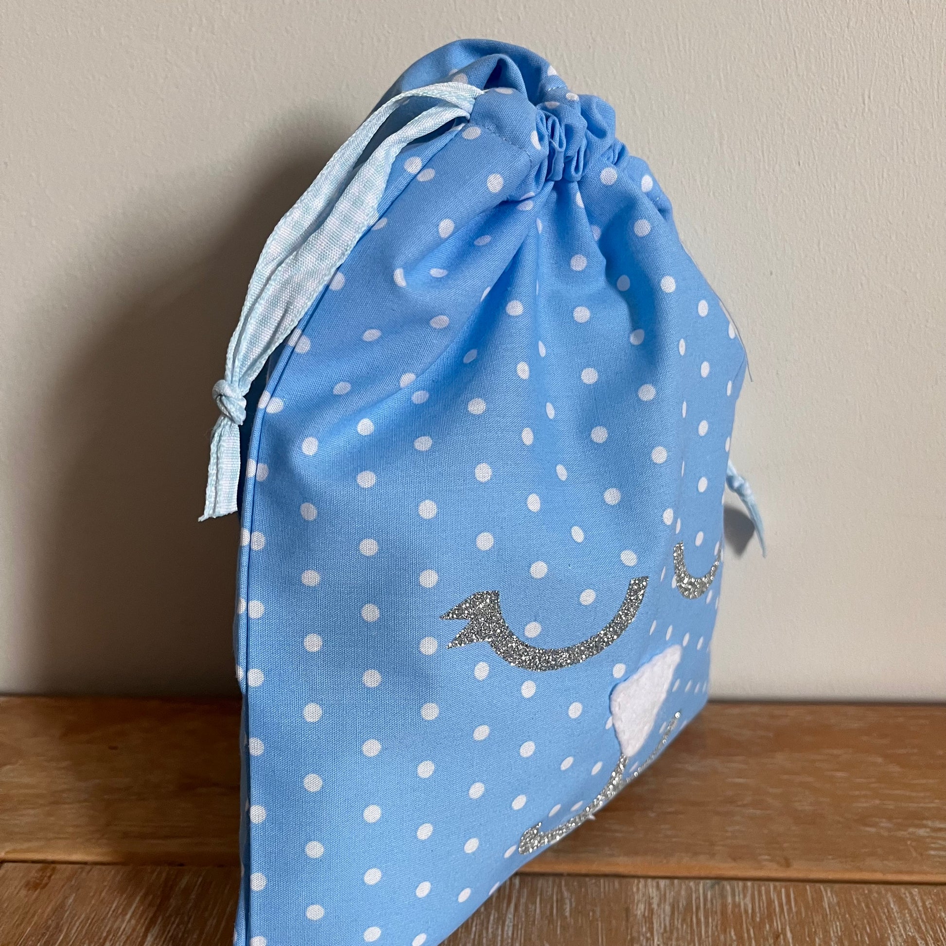 Blue polka dot drawstring bag with a glitter whale tail design