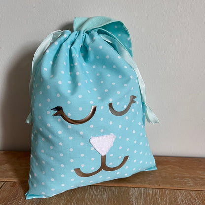 Blue polka dot drawstring bag with a white nose and brown eyes and mouth