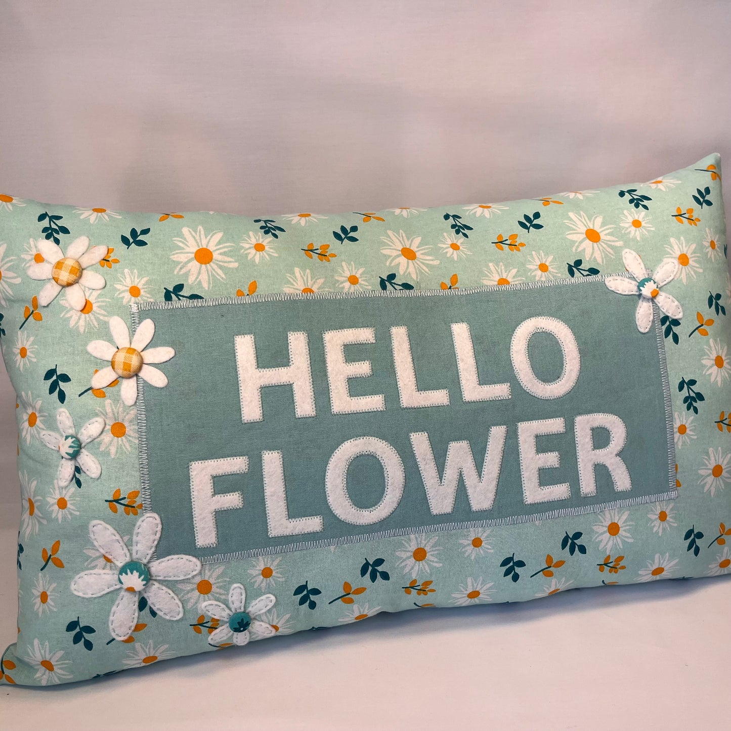 Hello Flower pillow with white felt letters and daisy print on a light blue background