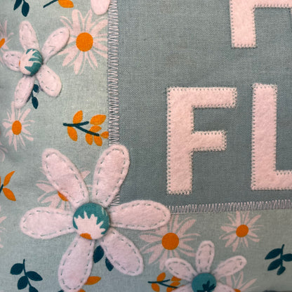 Close up of a light blue fabric with white daisies and the letters F and L in white