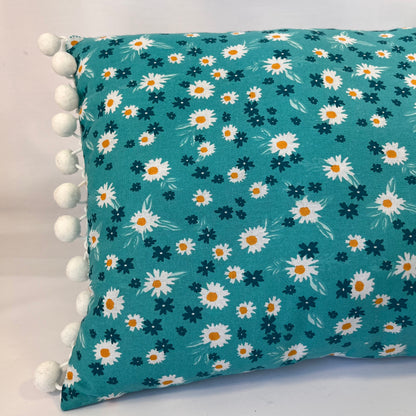 Teal pillow with white and orange daisy pattern and white pom-pom trim
